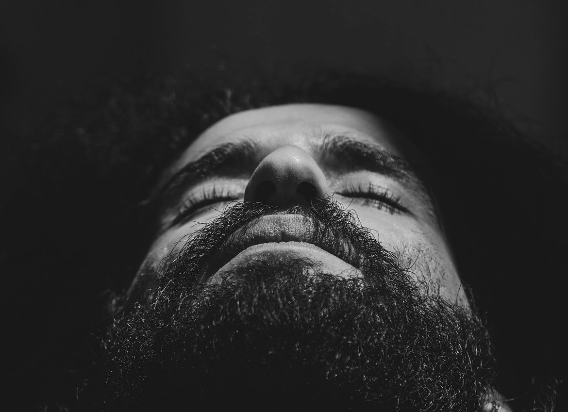 Visage extatique barbu Portrait en noir et blanc d’un homme barbu aux cheveux crépus, yeux fermés, bouche entrouverte, en gros plan sur son visage extatique vu de bas en haut, dans une ambiance sensuelle et mystérieuse.